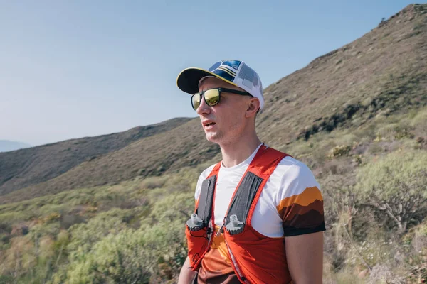 Sağlıklı beyaz bir adamın açık havada duran ve gülümseyen portresi. Taşra yolunda kendinden emin genç bir koşucu..