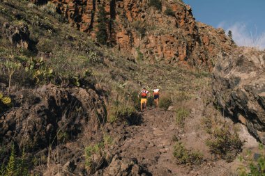 Bir grup genç yetişkin doğadaki yamaçlarda birlikte antrenman yapıyor ve birlikte koşuyorlar. Zinde genç insanlar dağ yolunda koşuyor..