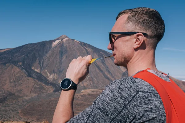 Porträt eines jungen Mannes, der nach dem Trailrunning im Sitzen und Ruhen Sport-Nährstoff-Gel isst lizenzfreie Stockfotos