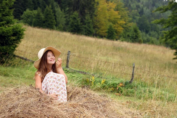 幸せな女の子は夏のシーズンの干し草に座っています — ストック写真