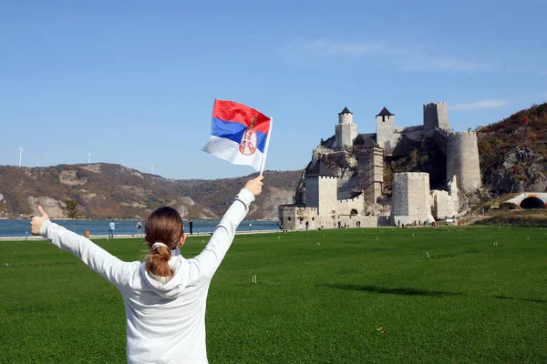 a girl with a Serbian flag and thumb up looks at the Golubac fortress