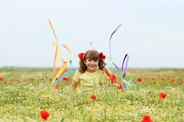 Fröhliche kleine Mädchen Spaß und winken mit bunten Bändern auf der Wiese — Stockfoto