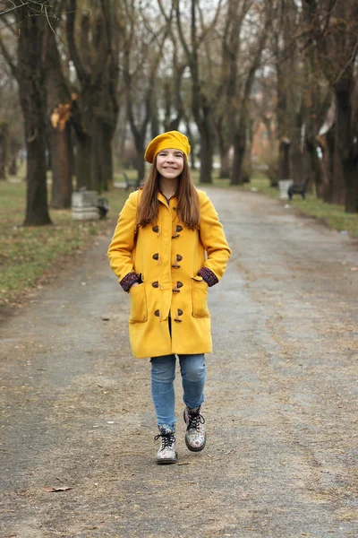 Щаслива дівчина-підліток в жовтому пальто, що йде в парку — стокове фото