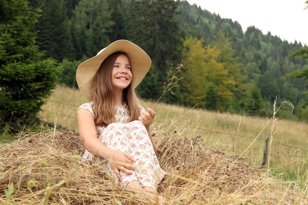 Happy little girl is sitting in the hay summer season — Stock Photo, Image