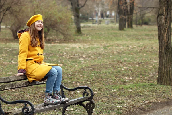 Adolescente está sentado en el banco en la temporada de otoño parque — Foto de Stock