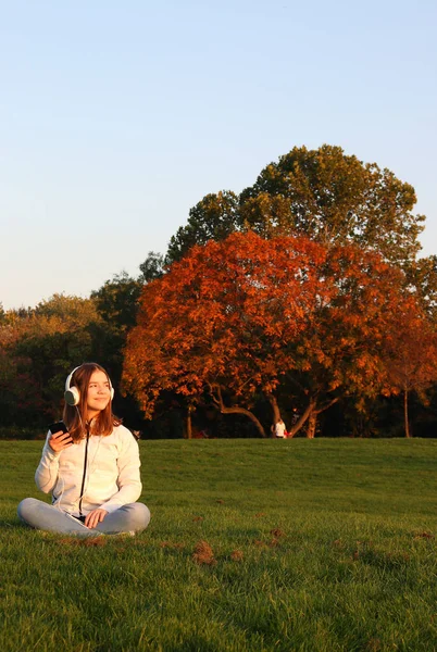 Teenage girl listens to music from her smartphone in park autumn — ストック写真