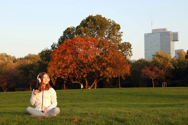 在秋天的公园里 少女用智能手机听音乐 — 图库照片