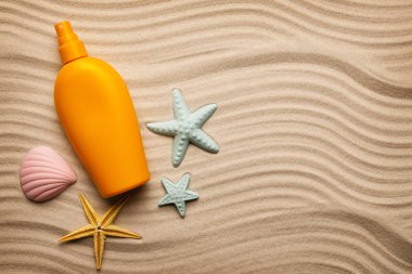 Sarı bir şişe ve sahilde deniz kabuklarını güneş yağı