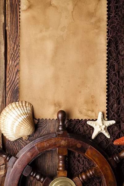 Blank paper sheet, shells and ship's steering wheel on brown fishing net and wooden background