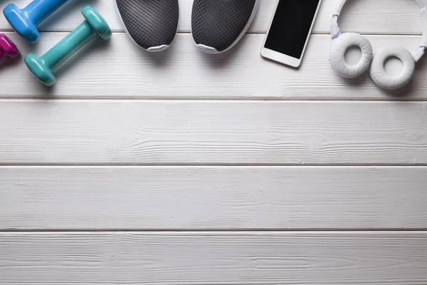 Fitness symbols - dumbbells, sports shoes and smartphone with headphones on a wooden background