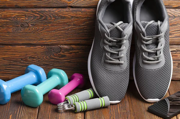 Sport accessories - colored dumbbells and sport shoes on wooden background