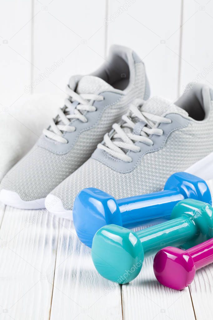 Sport and fitness symbols - Sports shoes, colorful dumbbells and white towel on wooden wall background