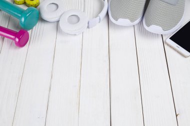 Smartphone, beyaz kulaklık, spor ayakkabı, renk dumbell ve ahşap masa üzerinde ölçüm bandı