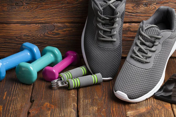 Sport accessories - colored dumbbells and sport shoes on wooden background