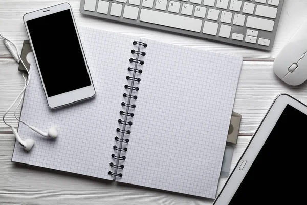 Modern smartphone, earphones, tablet and computer mouse, keyboard and notebook on white table