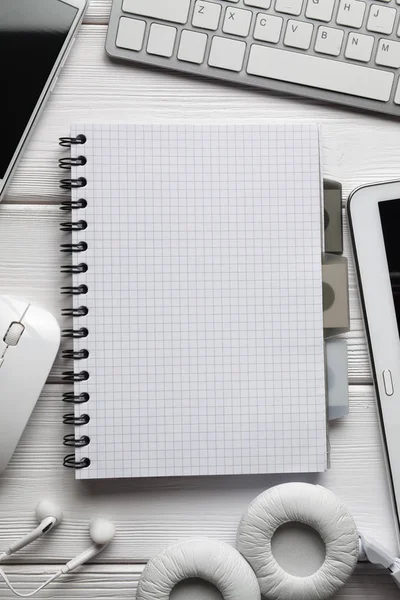 Notepad, headphones, smartphone and computer accessories on white wooden table