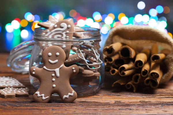 Gingerbread Christmas cookies in a jar and cinnamon sticks on lighting background and wooden table