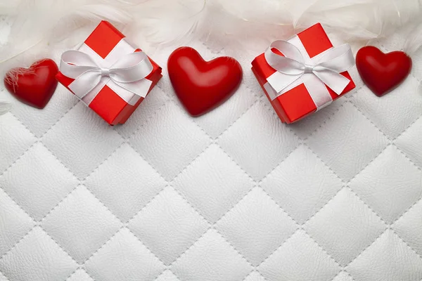 两个红色礼品盒与白色丝带 羽毛和三个红色心脏在白色棉被皮革背景 — 图库照片