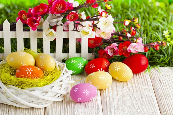 Барвисті великодні яйця на білому дерев'яному столі і квіти на траві — стокове фото