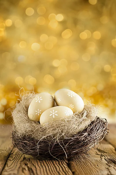 Ovos de Páscoa no ninho na mesa de madeira e costas abstratas douradas — Fotografia de Stock