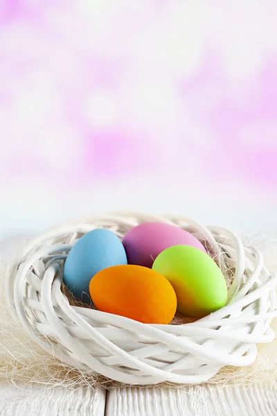 Quattro uova di Pasqua in nido bianco su tavola e sfondo astratto rosa — Foto Stock