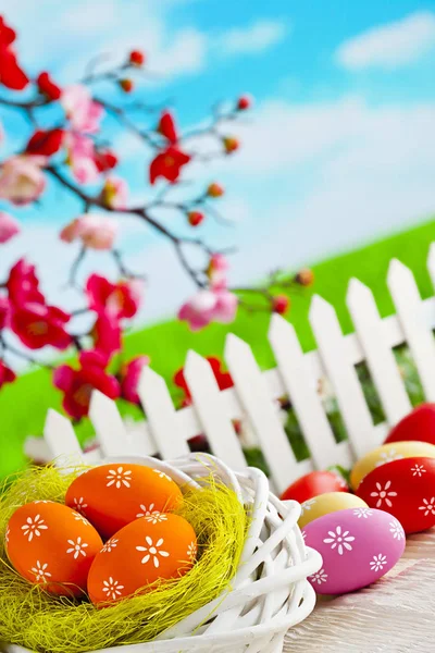 Kleurrijke paaseieren, nest en hek op houten tafel en natuur — Stockfoto