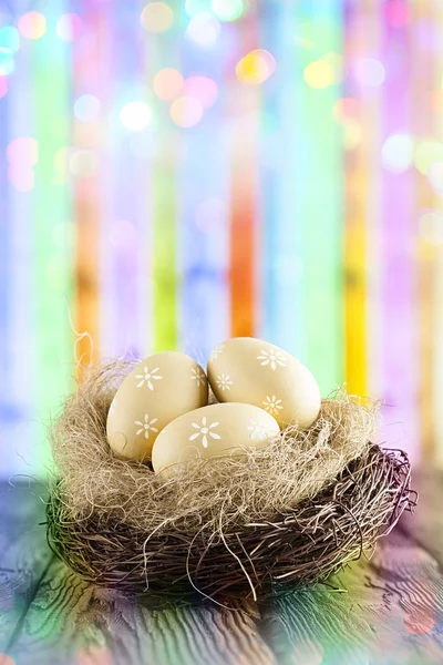 Ovos de Páscoa no ninho em mesa de madeira e ba abstrato colorido — Fotografia de Stock