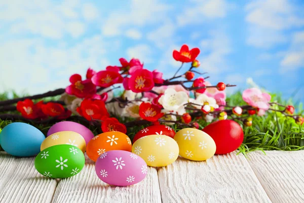 木桌上五颜六色的复活节彩蛋和树枝上有鲜花 — 图库照片