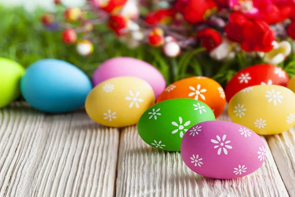 Colorful painted Easter eggs and flowers on wooden table and gra — Stock Photo, Image