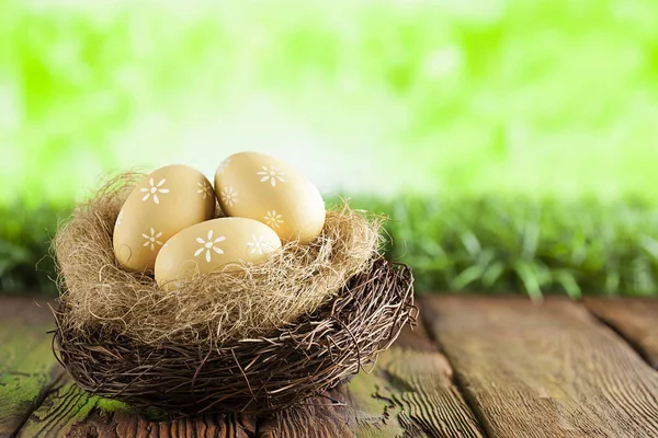 Tři malované velikonoční vajíčka v hnízdě na stůl a zelená příroda — Stock fotografie