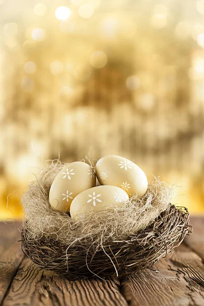 Пасхальные яйца в гнезде на деревянном столе и золотой абстрактный обратно — стоковое фото