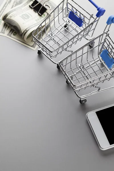 Two shopping carts, modern mobile phone and dollar bills on a gr — Stock Photo, Image
