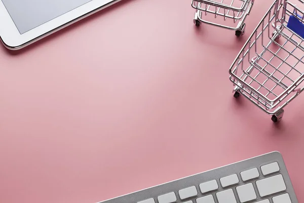 Einkaufswagen, Computertastatur und modernes Tablet auf rosa Rückseite — Stockfoto