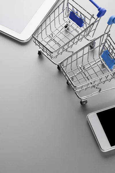 Twee winkelwagentjes, moderne mobiele telefoon en Tablet op een grijs BAC — Stockfoto