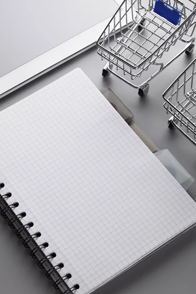 Twee winkelwagentjes, een notebook met een blanco pagina en een moderne mobiele — Stockfoto