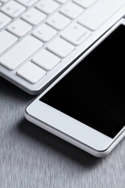 Gri bir alümina üzerinde modern beyaz cep telefonu ve bilgisayar klavyesi
