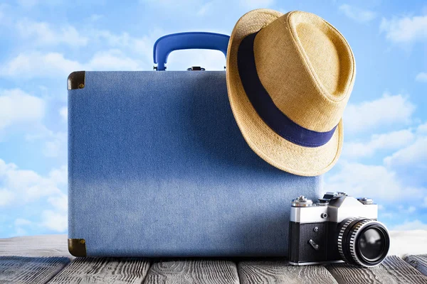 Modrý kufřík, letní klobouk a fotokamera na dřevěné kartě — Stock fotografie