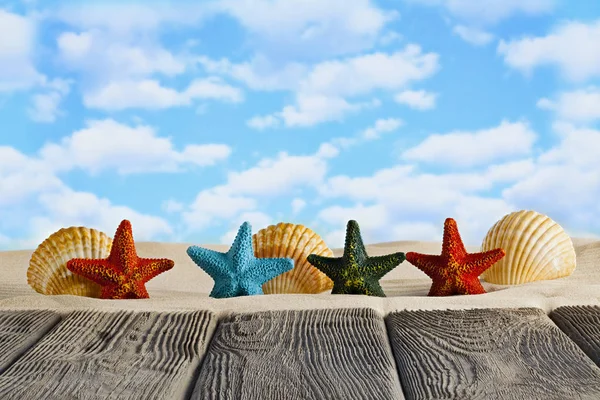 Estrelas coloridas e concha na areia da praia e mesa de madeira — Fotografia de Stock