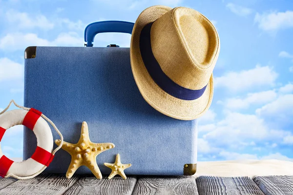 Ahşap masa ve plaj kumu üzerinde seyahat çantası ve yazlık şapka — Stok fotoğraf