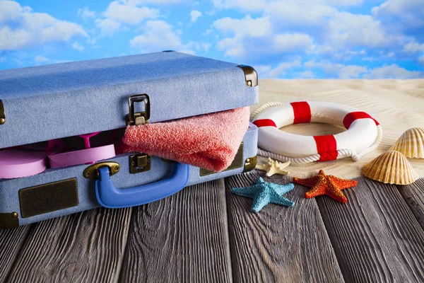 Offener Urlaubskoffer; Handtuch, Flip Flops, Rettungsring und Muscheln an — Stockfoto