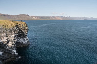 Su geçirmez ceket kız uçurumdaki İzlanda okyanusta arka plan üzerinde duruyor. İzlanda için seyahat