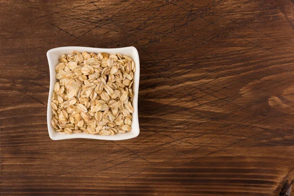 Yulaf veya yulaf gevreği kapta ahşap arka plan üzerinde yuvarlandı. Sağlıklı yaşam tarzı, sağlıklı beslenme kavramı. Üstten görünüm 