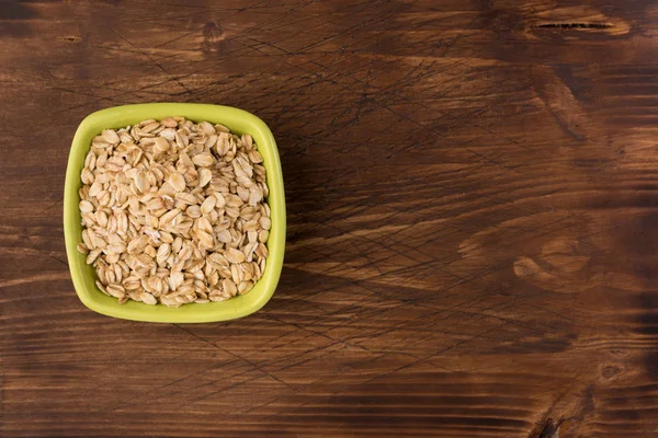 Yulaf veya yulaf gevreği kapta ahşap arka plan üzerinde yuvarlandı. Sağlıklı yaşam tarzı, sağlıklı beslenme kavramı. Üstten görünüm 