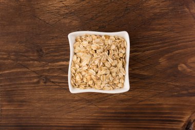 Yulaf veya yulaf gevreği kapta ahşap arka plan üzerinde yuvarlandı. Sağlıklı yaşam tarzı, sağlıklı beslenme kavramı. Üstten görünüm 