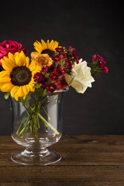 Karanlık bir arka plan üzerinde bir vazoda beyaz sarı ve kırmızı çiçekler Buket