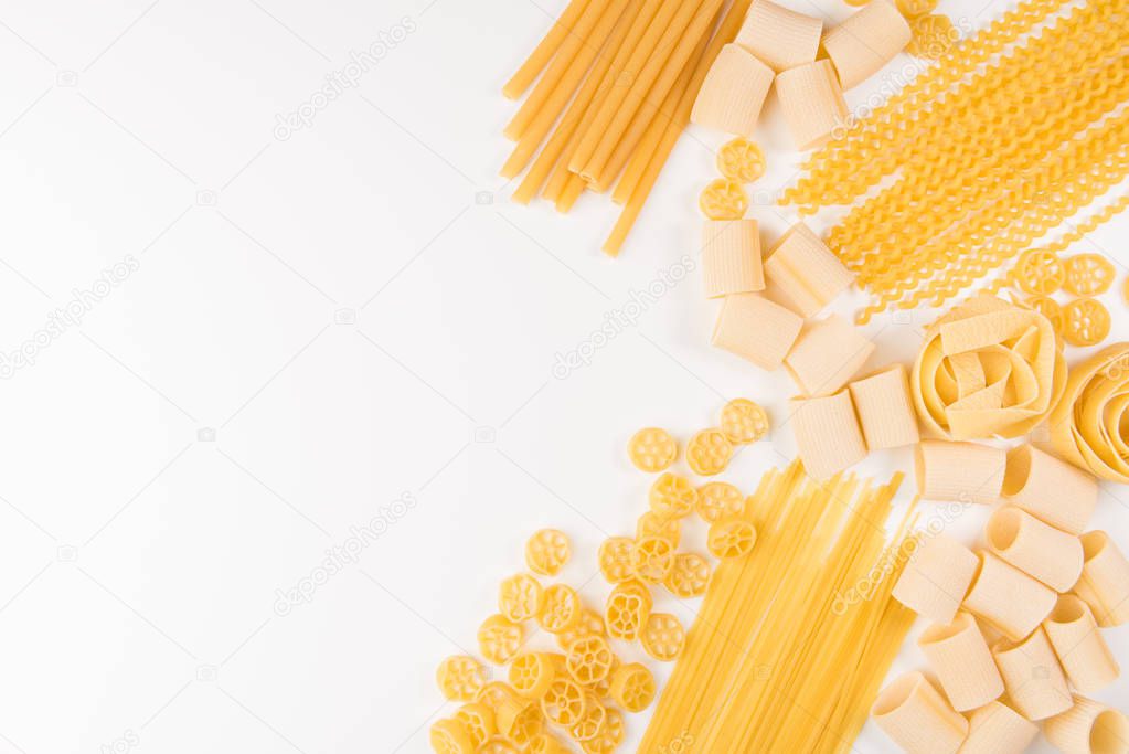 An overhead photo of different types of pasta, including spaghetti, penne, fusilli, and others, flay lay on a white background with a place for text