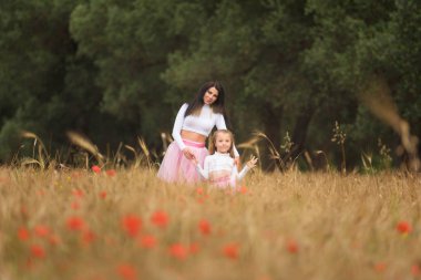 Genç bir anne kızının eğleniyor ve buğday alanlarında poz ile