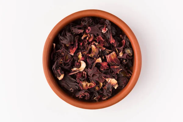 petals of dry hibiscus tea  in the clay pot isolated on white background, top view