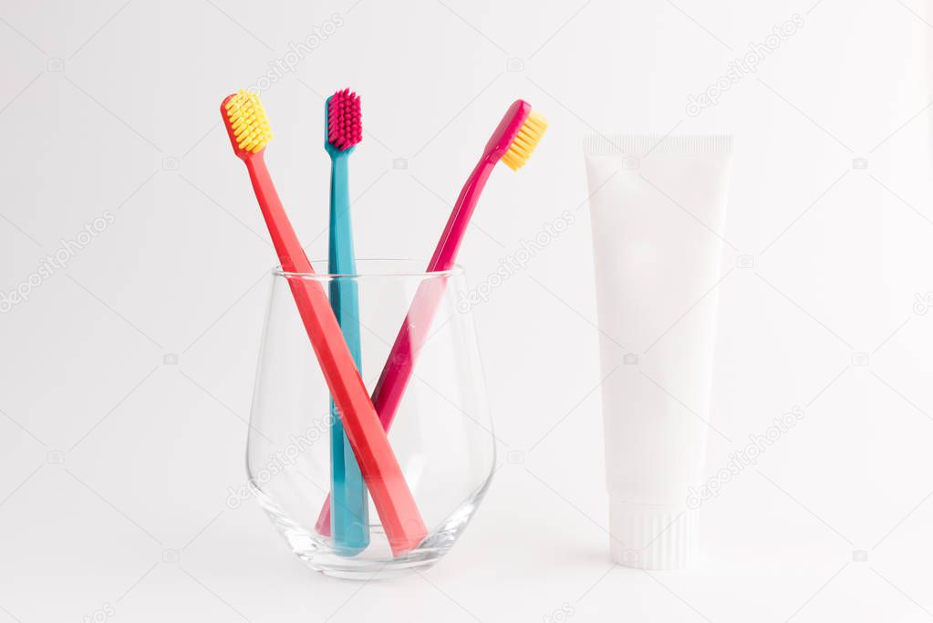Toothbrushes in glass isolated on pink background with toothpaste tube