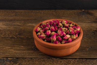 siyah arka plan üzerine ahşap masa üzerinde izole bir toprak kap içinde çay gül tomurcukları